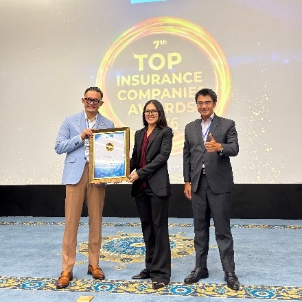 Three business professionals stand on a stage during an awards ceremony, with the central person holding a framed certificate. The backdrop displays the text "7th TOP INSURANCE COMPANIES AWARDS 2026" inside a glowing circular graphic. The setting appears to be a formal corporate event in a conference hall, with a patterned blue carpet and presentation screen. The mood is celebratory and professional, highlighting recognition and achievement in the insurance industry.